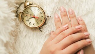 Mains soignées avec une manucure en gel rose nude longue tenue posées à côté d'un réveil rétro