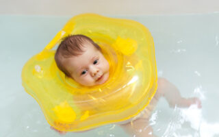 Nourrisson qui flotte calmement dans l'eau d'un baby spa avec une bouée de cou jaune pour améliorer son sommeil
