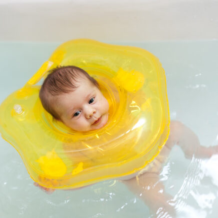 Nourrisson qui flotte calmement dans l'eau d'un baby spa avec une bouée de cou jaune pour améliorer son sommeil