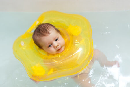 Nourrisson qui flotte calmement dans l'eau d'un baby spa avec une bouée de cou jaune pour améliorer son sommeil