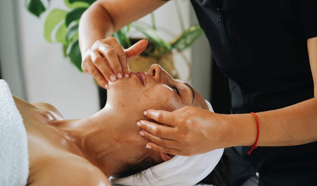 Esthéticienne réalisant un massage facial Kobido anti-âge et un drainage du visage en institut