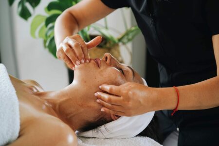 Esthéticienne réalisant un massage facial Kobido anti-âge et un drainage du visage en institut